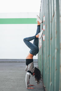 Full length of female athlete doing handstand on street by cargo container