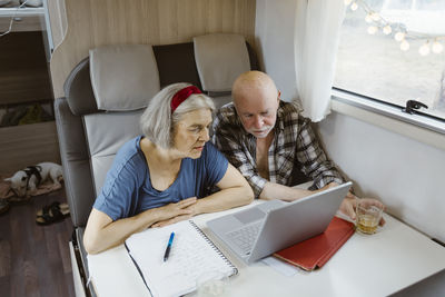 Curious senior couple sitting with laptop at table in camper van