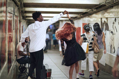 Happy couple dancing while street musician singing in subway