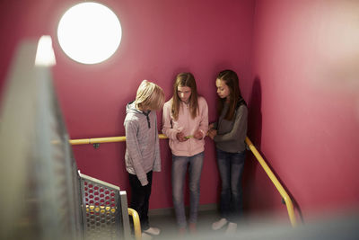 Girl using mobile phone with friends against pink wall in middle school
