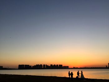 Silhouette people on beach against clear sky during sunset