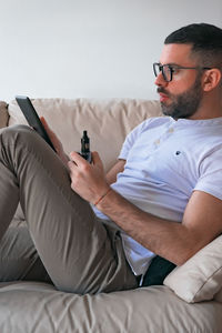 Man smoking while using digital tablet on sofa at home