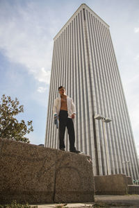 Man with fully unbuttoned shirt standing against modern building in city