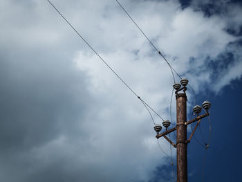 Low angle view of telephone pole against cloudy sky