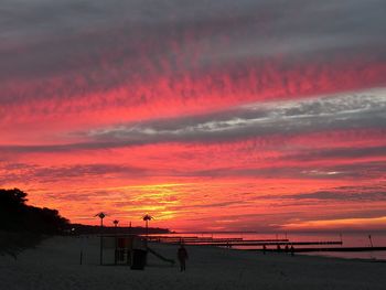 Silhouette people on beach against orange sky