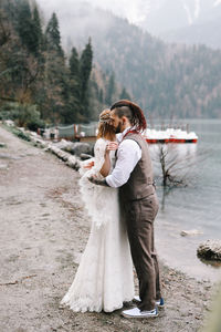 Happy newlyweds in love a man and a woman in wedding clothes embrace on the shore of the lake