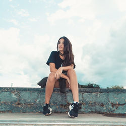 Portrait of young woman sitting against sky