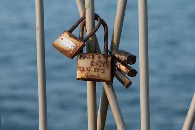 Close-up of rusty love locks on railing against seascape