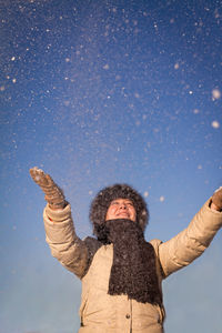 Woman enjoying snowfall while standing against sky during winter