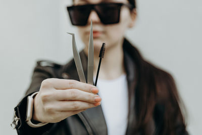 The girl shows tweezers and a brush for eyelash extensions.