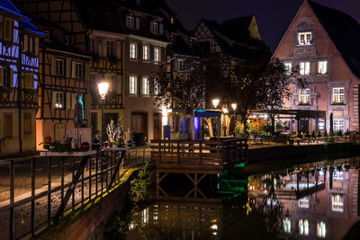 Illuminated bridge over canal amidst buildings in city at night