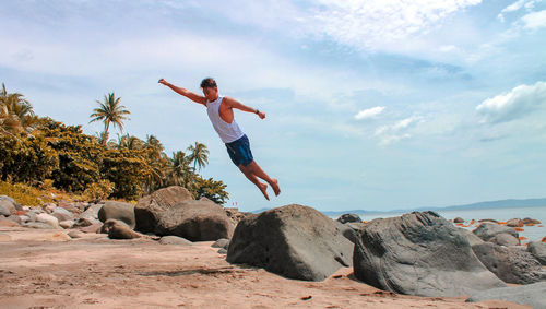 Full length of man jumping on rock at beach against sky