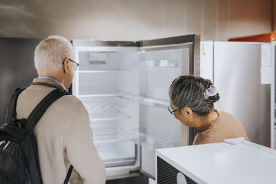 Senior couple opening and examining refrigerator while shopping in appliances store