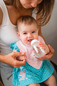 Mother helps her daughter to drink water. child learns to hold a bottle.