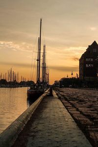 Sailboats moored at harbor against sky during sunset