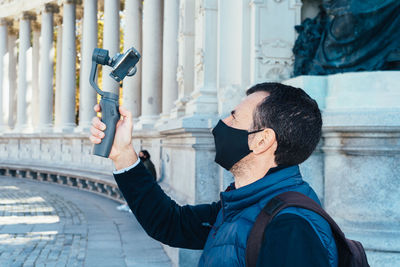 Man wearing face mask holding a gimbal with a phone filming monuments in madrid