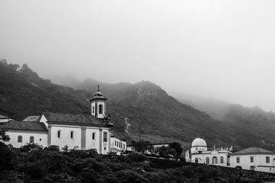 Low angle view of buildings and mountain against sky in foggy weather