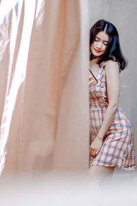 Woman looking away while standing against curtain