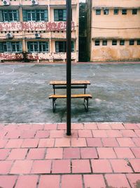 Empty bench on sidewalk by street in city