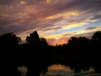 Silhouette trees by lake against sky during sunset