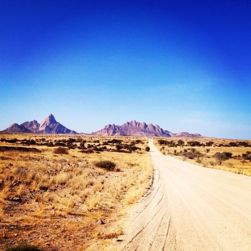 the way forward, clear sky, landscape, tranquil scene, desert, copy space, mountain, tranquility, blue, road, diminishing perspective, arid climate, country road, scenics, dirt road, vanishing point, non-urban scene, nature, mountain range, beauty in nature