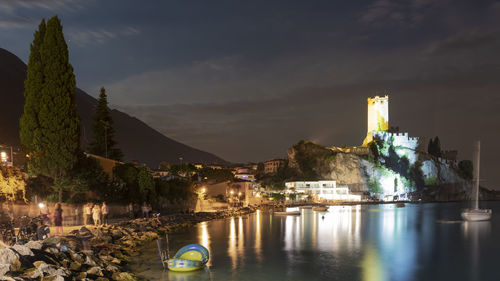 Illuminated buildings by river against sky at night