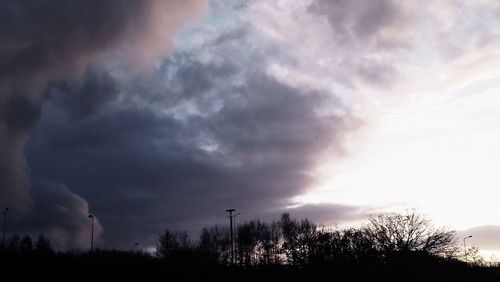 Low angle view of silhouette trees against storm clouds