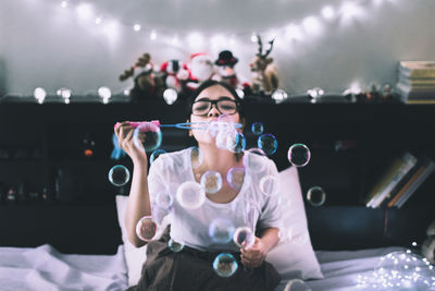 Young woman blowing bubbles on bed at home
