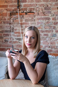 Portrait of happy blonde young woman drinking her cappuccino while relaxing at a table in a cafe