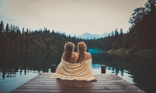 Rear view of woman sitting by lake against sky