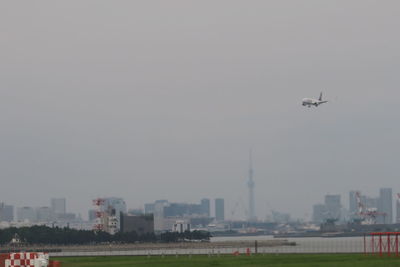 Airplane flying over buildings in city against clear sky