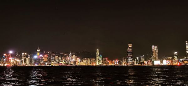 Illuminated buildings by river against sky at night
