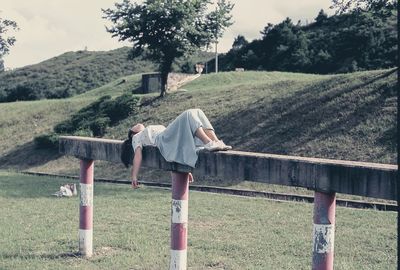 Full length of woman relaxing on wooden post in park