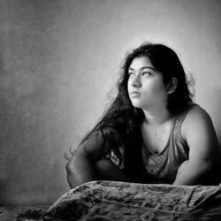 Portrait of woman sitting on bed against wall at home