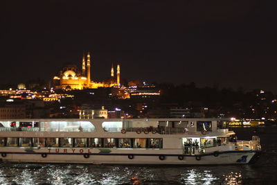 Illuminated city by sea against sky at night