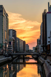 Bridge over river by buildings against sky during sunset