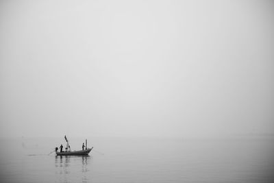 Two people in boat over sea against clear sky