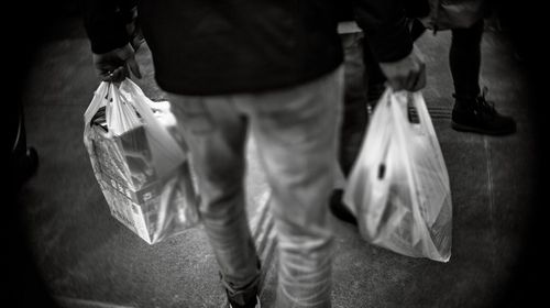 Low section of man carrying plastic bags while walking on footpath