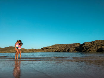 Girls standing on beach against clear sky