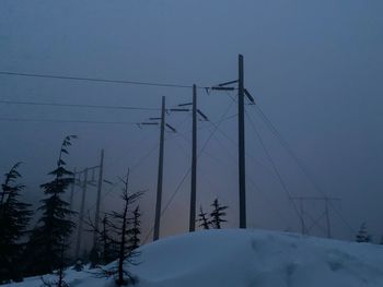 Low angle view of snow covered electricity pylon against sky