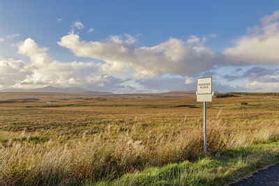 Road sign on field against sky