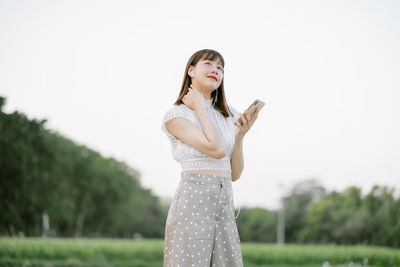 Young woman holding smart phone and looking away while standing on land