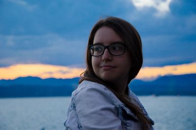 Smiling young woman looking away against sea during sunset