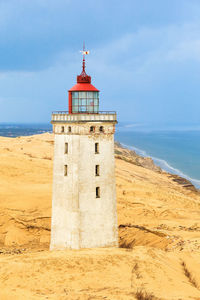 Lighthouse on beach against sky