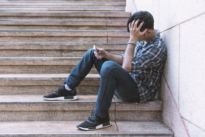 Side view of young man using mobile phone while sitting on steps