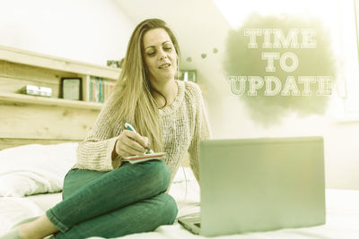 Young woman using mobile phone while sitting on laptop