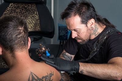 Artist making tattoo on shirtless man shoulder