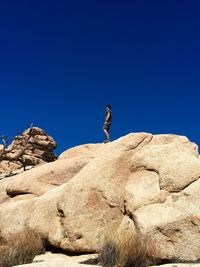 Low angle view of male hiker standing on rock formation against clear blue sky