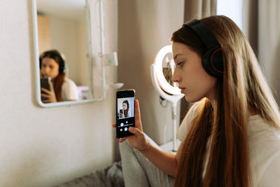 Teenage girl in headphones in front of the mirror takes selfie, admires.