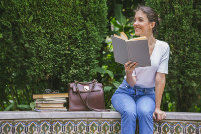 Young woman sitting on seat against plants